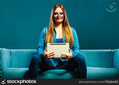 Modern technologies leisure and young people concept. fashionable woman wearing jeans with tablet sitting on couch blue color