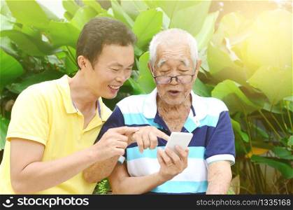 Modern technology, age and people concept. Asian family using smart-phone. Family living lifestyle at garden.