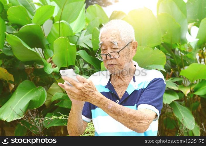 Modern technology, age and people concept. Asian Senior man using smart-phone at garden.