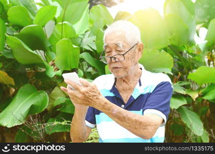 Modern technology, age and people concept. Asian Senior man using smart-phone at garden.