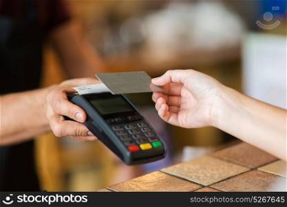 modern technology and people concept - man or bartender with payment terminal and customer hand with credit card at bar of coffee shop. hands with payment terminal and credit card