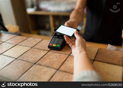 modern technology and people concept - man or bartender with payment terminal and customer with smartphone at bar of coffee shop. hands with payment terminal and smartphone at bar