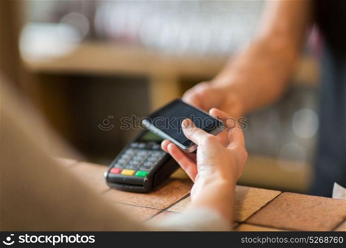 modern technology and people concept - man or bartender with payment terminal and customer with smartphone at bar of coffee shop. hands with payment terminal and smartphone at bar
