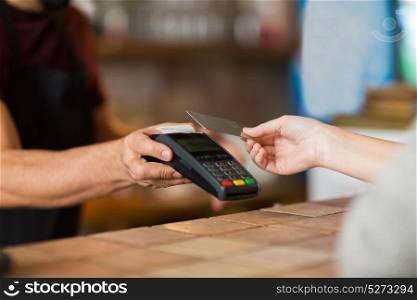 modern technology and people concept - man or bartender with payment terminal and customer hand with credit card at bar of coffee shop. hands with payment terminal and credit card
