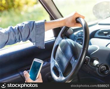 Modern technology concept. Man using mobile phone while driving car, checking social media or setting navigation.. Man using his phone while driving car.
