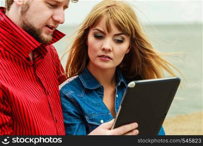 Modern technology devices and tourism concept. Young couple outdoor against sea water with tablet enjoying summer holidays