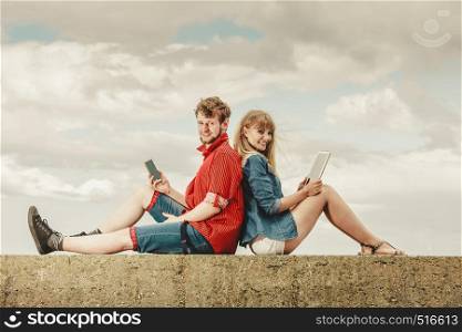 Modern technology devices. Young couple outdoor against sky man with smartphone, woman with tablet enjoying summer holiday