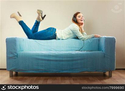 Modern technology leisure and happiness concept. Young woman with headphones laying on couch using tablet listening music