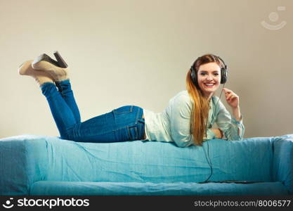 Modern technology leisure and happiness concept. Young woman with headphones laying on couch using tablet listening music