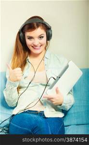 Modern technology leisure concept. Young attractive woman with headphones relaxing using tablet making thumb up hand sign gesture