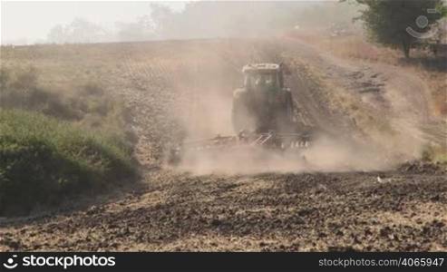 Modern tractor with harrows harrowing field, long shot tilt up
