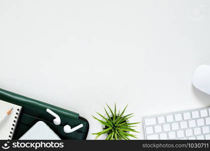 Modern workplace with wireless keyboard and mouse, smartphone with wireless earphones, pencil, notebook, green document bag and Tillandsia air plant on white background. Top view, flat lay concept.