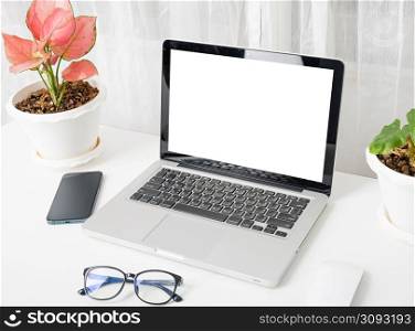 Modern workspace, mock up laptop computer blank white screen, eyeglasses and smartphone white table have potted plants on the desk, Notebook and mobile phone on desktop home office