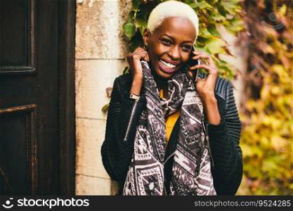 Modern young african american woman holding mobile hone and smiling at autumn outdoor