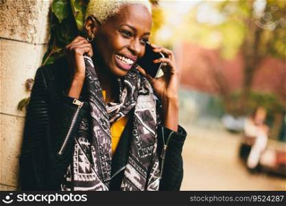 Modern young african american woman holding mobile hone and smiling at autumn outdoor