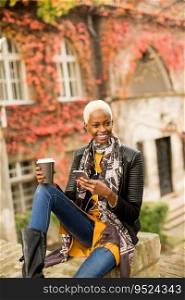 Modern young african american woman posing with coffee to go and mobile phone outdoor