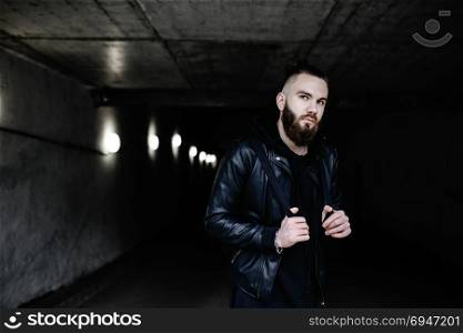 Modern young bearded man in black style clothes standing in around urban background.. Modern young bearded man in black style clothes standing in around urban background