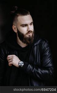 Modern young bearded man in black style clothes standing in urban background.. Modern young bearded man in black style clothes standing in urban background