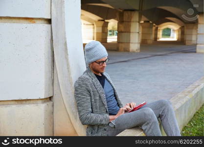 Modern young man with tablet pc touch working under a bridge with wool winter cap