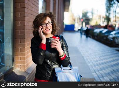 Modern young woman with coffee cup in hand talking on the mobile phone , urban background