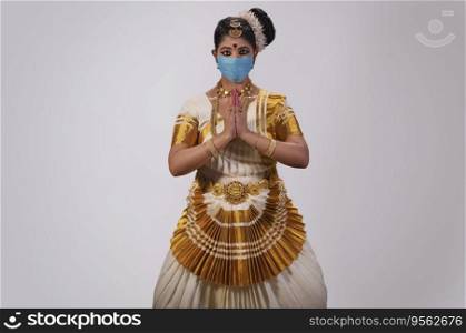 Mohiniattam dancer in a face mask standing with her hands joined