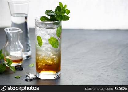 mojito cocktail, cold drink with ice cubes and fresh mint leaves on rustic dark table.