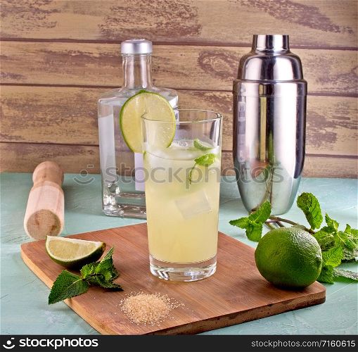 Mojito cocktail decorated with lime, mint leaves, ice cubes and silver shaker. Shaker, lemon, lime, mint leaves and ice for summer cocktail