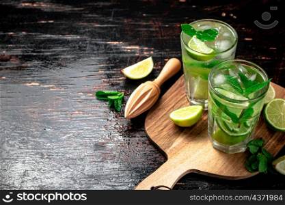 Mojito with pieces of lime on a cutting board. On a rustic dark background. High quality photo. Mojito with pieces of lime on a cutting board.