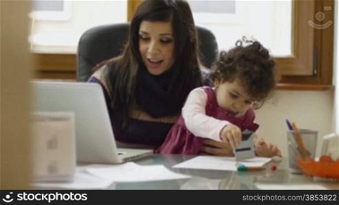 Mom and businesswoman working with laptop computer at home and playing with her baby girl
