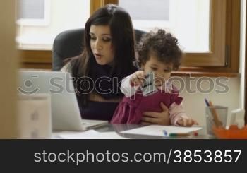 Mom and businesswoman working with laptop computer at home and playing with her baby girl