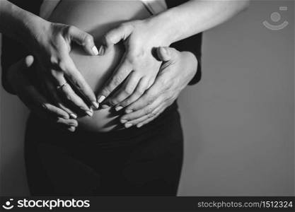 Mom and dad mother and father couple making a hart shape hands holding over the pregnant woman belly waiting for baby son or daughter to be born black and white