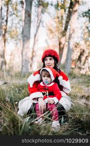 Mom and daughter disguised to christmas rest seating on the forest
