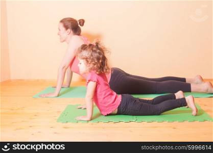 Mom and daughter doing yoga exercises on green rug. Wellness yoga exercises