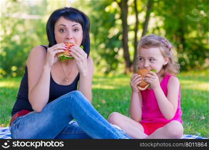 Mom and daughter eating tasty burgers on a picnic