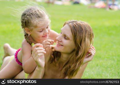 Mom and daughter having fun lying on a green lawn in the summer