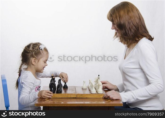 Mom and daughter playing at a table in chess. Mother teaches daughter game