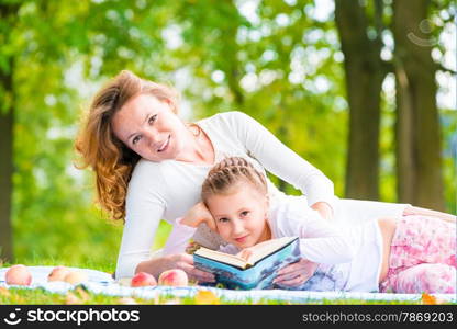 Mom and daughter reading a book lying in the park