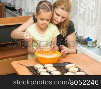 Mom and daughter seven years pour the batter into the mold for baking muffins