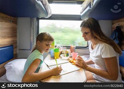 Mom and daughter sit at the table in the train and solve the puzzle in the children's magazine