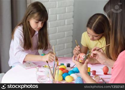 Mom and daughters enthusiastically paint Easter eggs at home