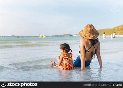 Mom and her kid are looking for the sunset on the beach at the evening.