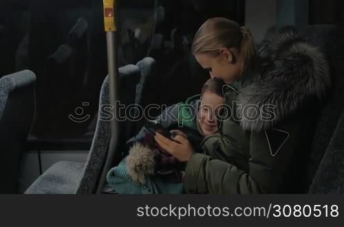 Mom and son having a night bus ride. To pass the time they using mobile. Woman and kid smiling as they looking through the photos