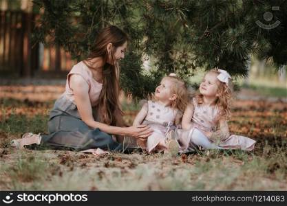 mom and two daughters are sitting in a meadow and reading a book. happy family, mom and two daughters. Mother&rsquo;s day concept.. mom and two daughters are sitting in a meadow and reading a book. happy family, mom and two daughters. Mother&rsquo;s day concept