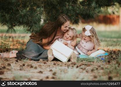 mom and two daughters are sitting in a meadow and reading a book. happy family, mom and two daughters. Mother&rsquo;s day concept.. mom and two daughters are sitting in a meadow and reading a book. happy family, mom and two daughters. Mother&rsquo;s day concept