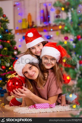 Mom and two daughters lie on the floor of a Christmas tree in the New Year&rsquo;s interior