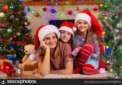 Mom and two daughters lie on the floor of a Christmas tree