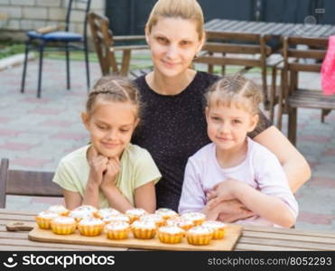 Mom and two daughters sitting at a table on which lay cooked them Easter cupcakes