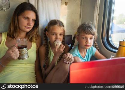 Mom and two girls are looking at the laptop screen in the train car, having a bite while