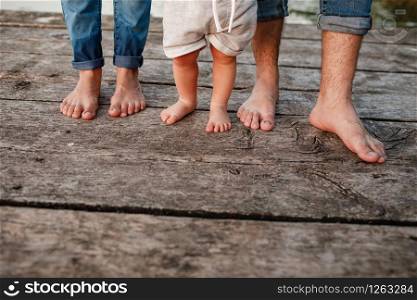 Mom, dad and baby walk bare feet on the wooden bridge. Happy young family spending time together, running outside, go in nature, on vacation, outdoors. The concept of family holiday. copy space.. Mom, dad and baby walk bare feet on the wooden bridge. Happy young family spending time together, running outside, go in nature, on vacation, outdoors. The concept of family holiday. copy space