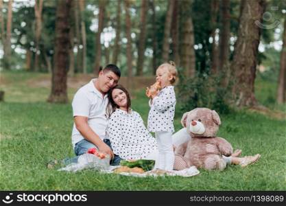 Mom, dad and little daughter on the picnic with teddy bear in the park outdoors. The concept of summer holiday. Mother&rsquo;s, father&rsquo;s, baby&rsquo;s day. Family spending time together on nature. Family look.. Mom, dad and little daughter on the picnic with teddy bear in the park outdoors. The concept of summer holiday. Mother&rsquo;s, father&rsquo;s, baby&rsquo;s day. Family spending time together on nature. Family look